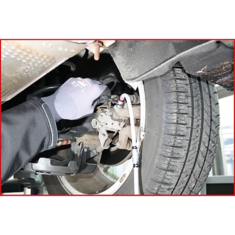 Nahaufnahme eines Mechanikers, der an einem Reifen arbeitet. Der Mann trägt Handschuhe. Das Bild zeigt einen Teil des Autos.